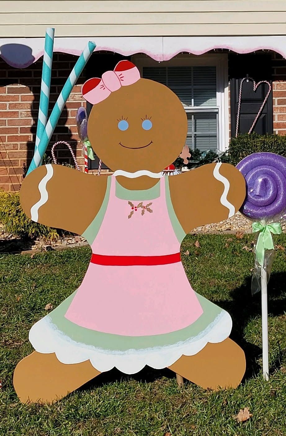 Gingerbread house decoration in pink dress holding blue candy canes and a purple lollipop lawn ornament