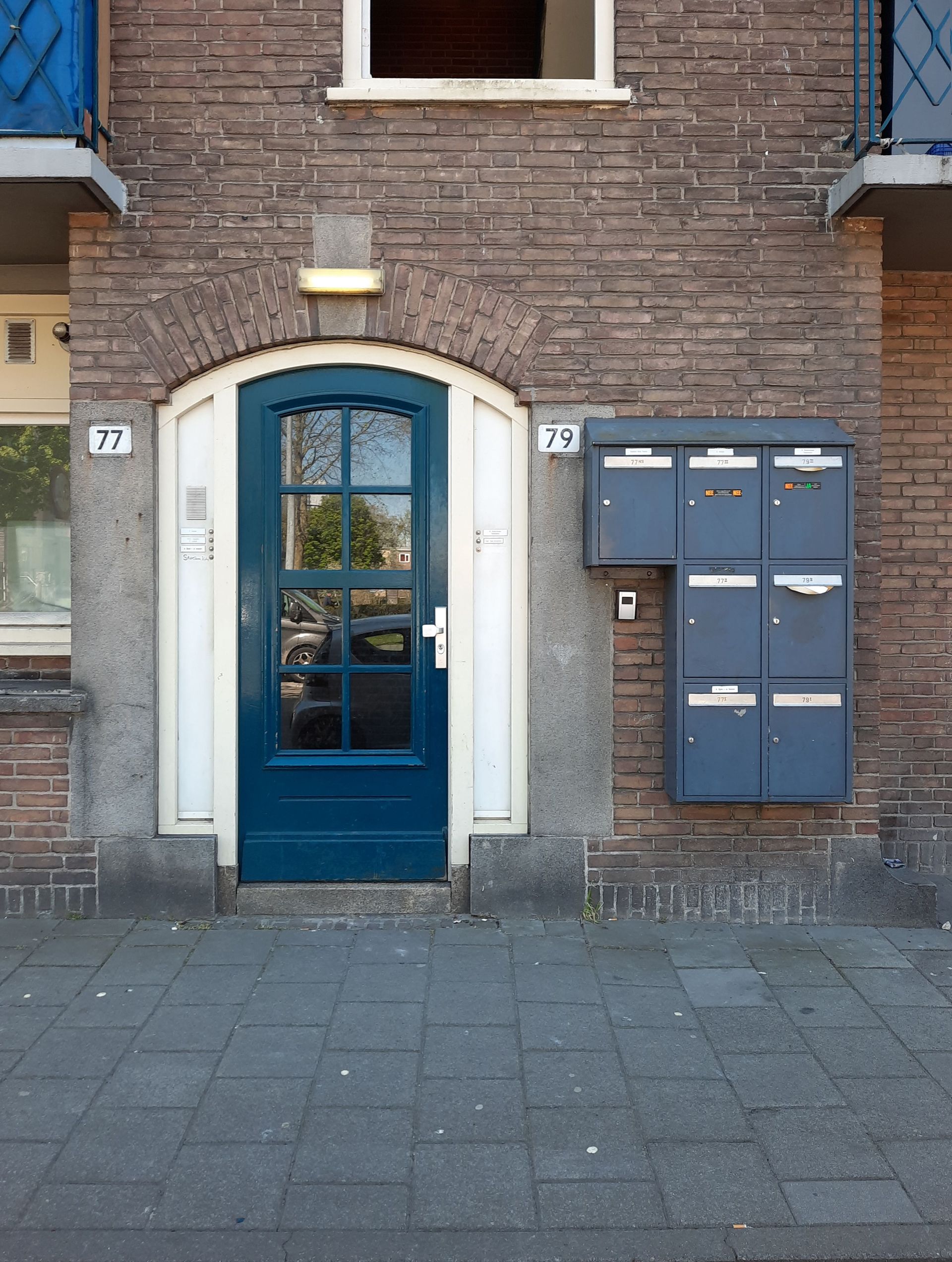 Brick building facade with blue door and mailboxes on a tiled sidewalk