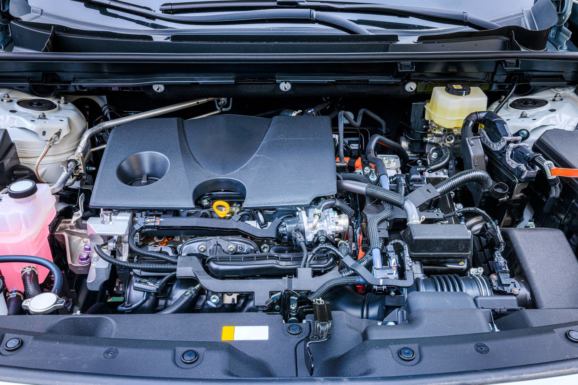 Car engine bay with plastic cover, battery, hoses, and fluid reservoirs under the hood. Car engine bay with plastic cover, battery, hoses, and fluid reservoirs under the hood.