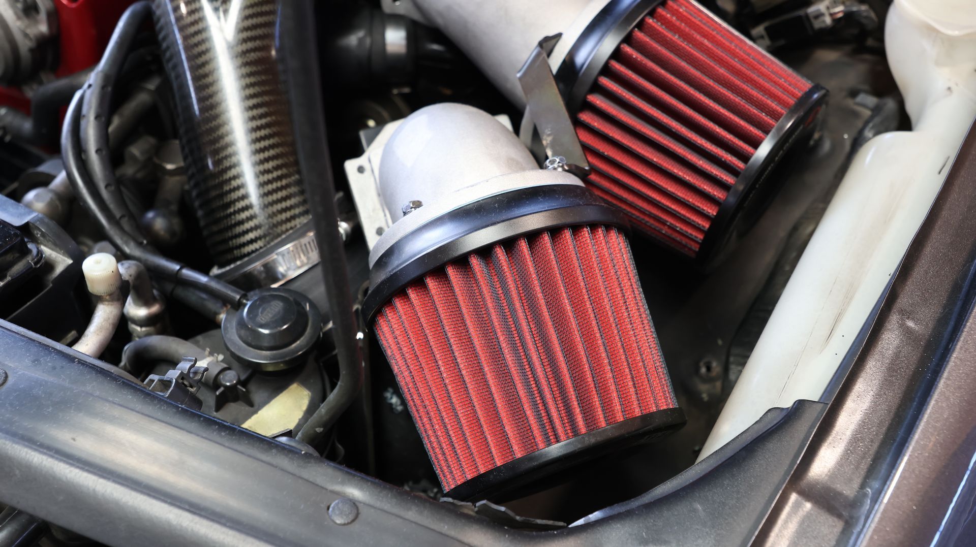Two red cone air filters in a car engine bay, one with a silver cap. Two red cone air filters in a car engine bay, one with a silver cap.