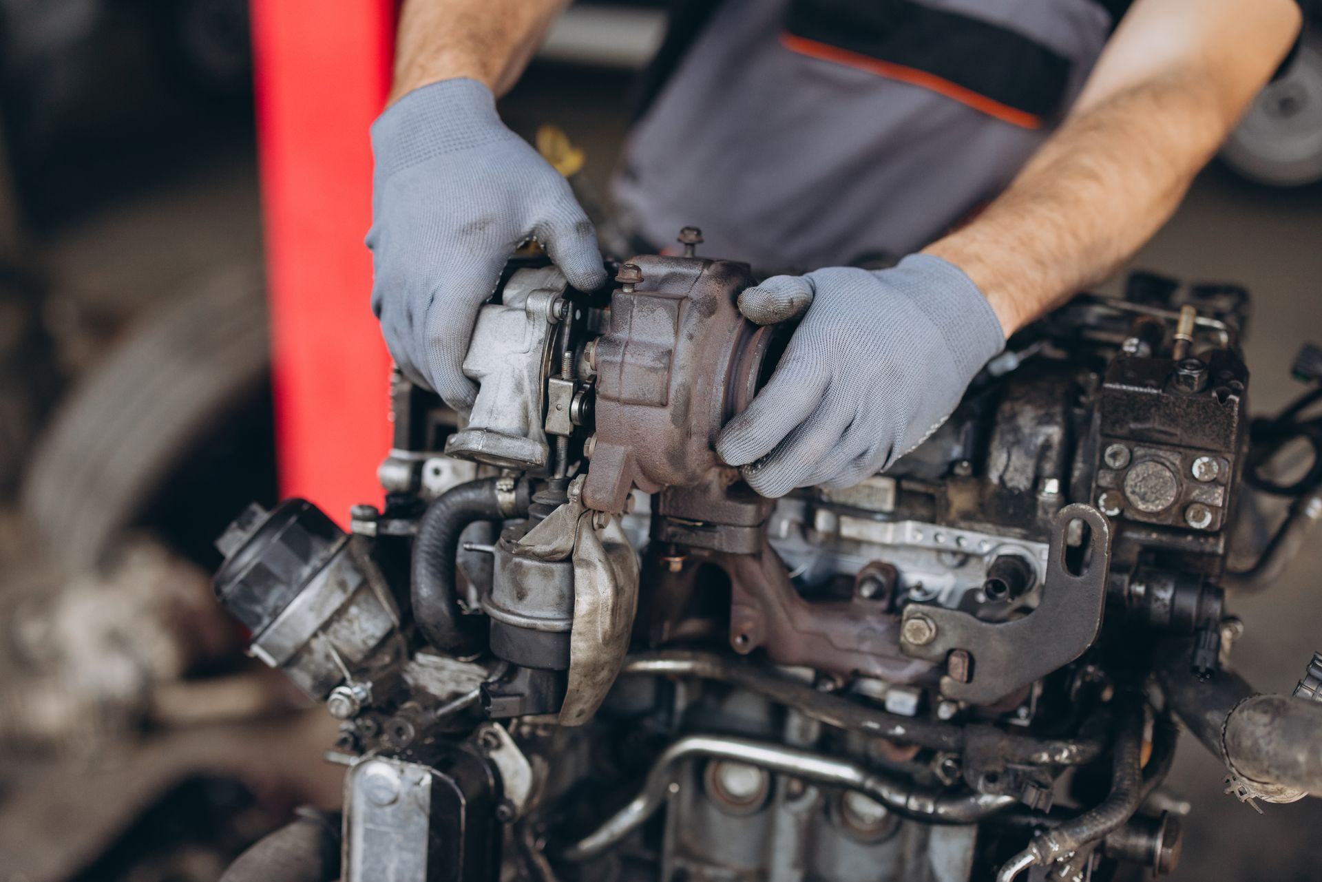 Mechanic wearing gray gloves repairs a rusty engine in a workshop Mechanic wearing gray gloves repairs a rusty engine in a workshop