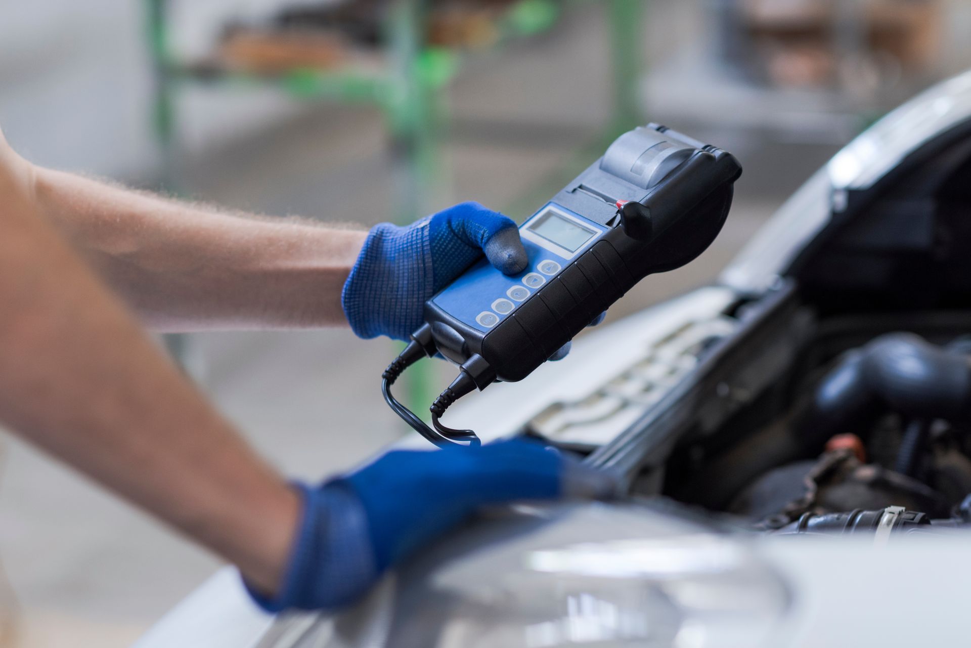 Mechanic in blue gloves using a handheld diagnostic tool on a car engine