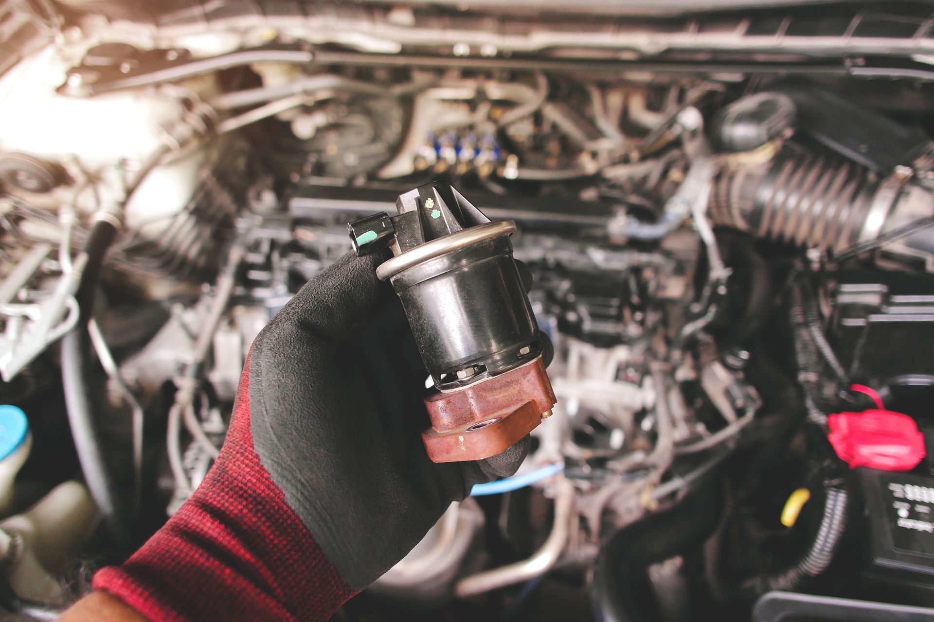 Gloved hand holding a small car engine part in an open engine bay Gloved hand holding a small car engine part in an open engine bay
