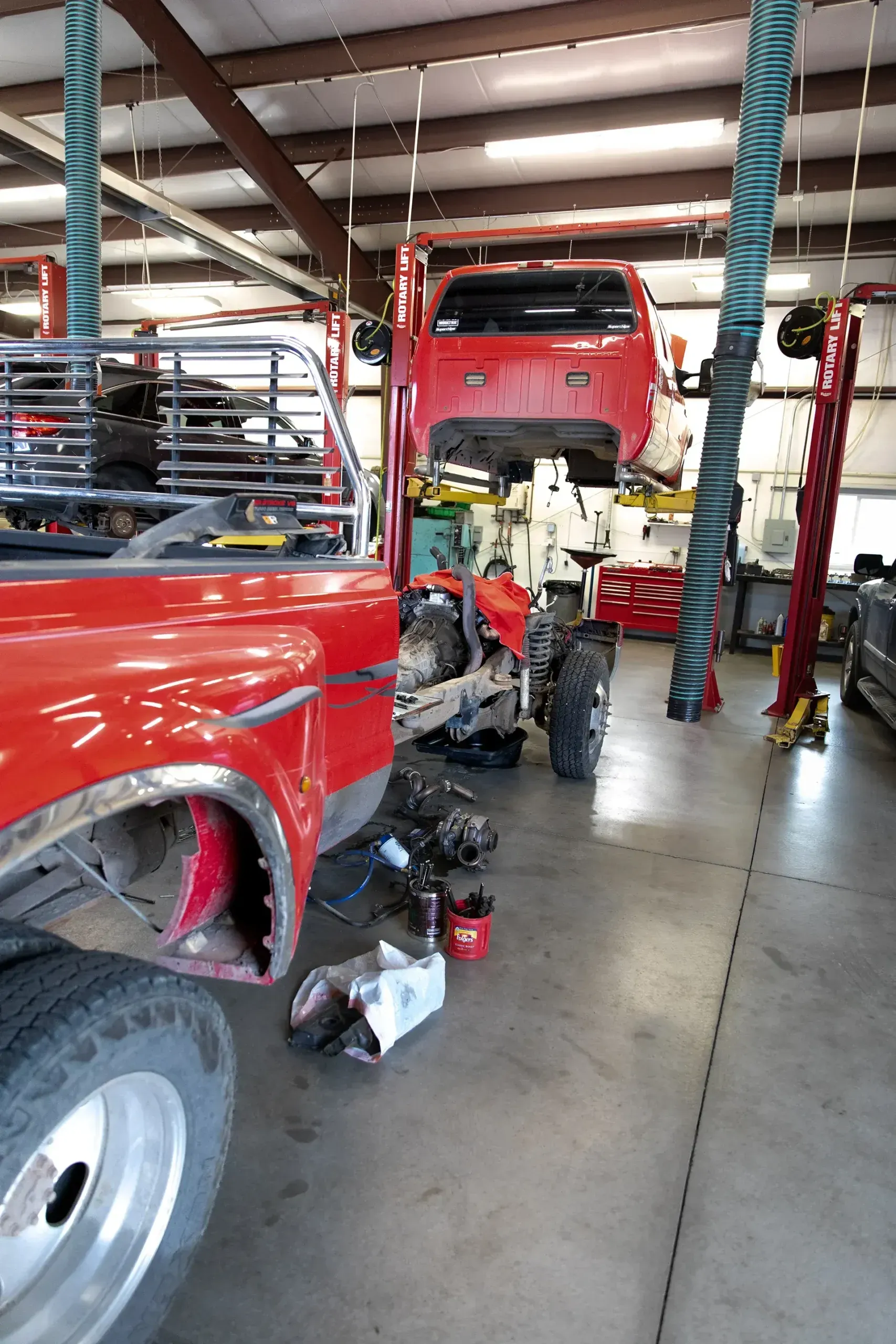 Red pickup truck in auto repair shop with mechanic working underneath and tools on the floor
