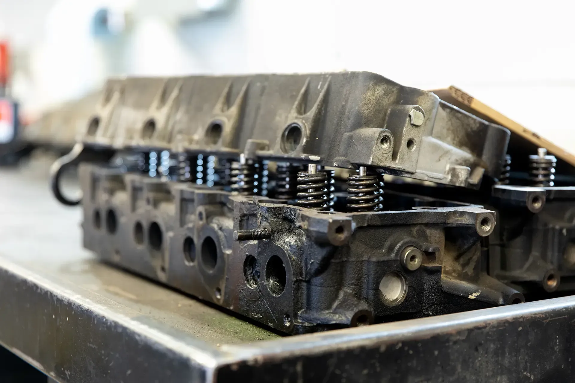 Metal engine cylinder head on a workbench, showing valve springs and machined ports. Metal engine cylinder head on a workbench, showing valve springs and machined ports.