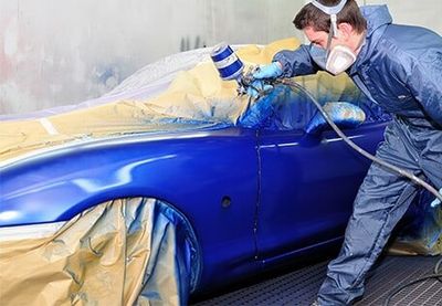 Man Wearing Blue Uniform Spray Painting a Car to Color Blue — Auto Body Repair Parma OH in Parma, OH