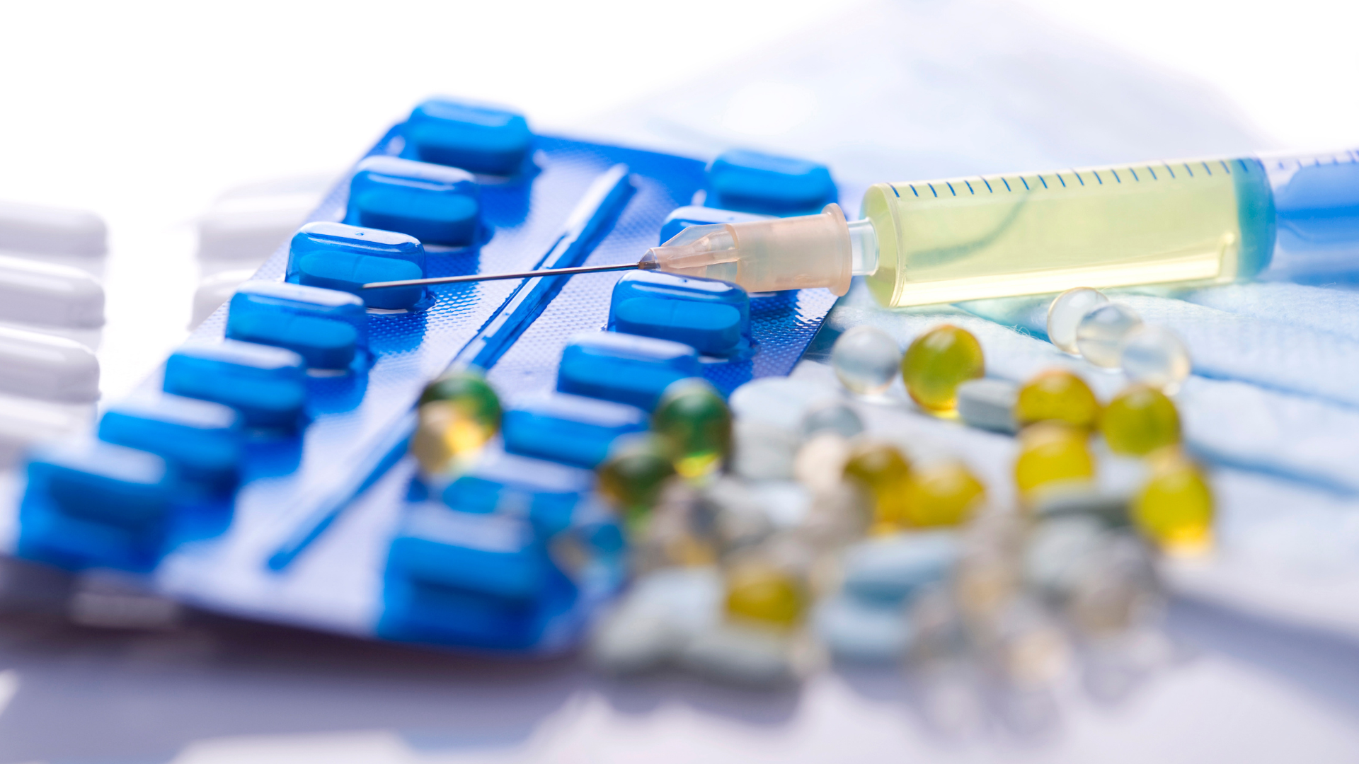 Blue pill blister packs with scattered yellow capsules and a syringe on a white surface