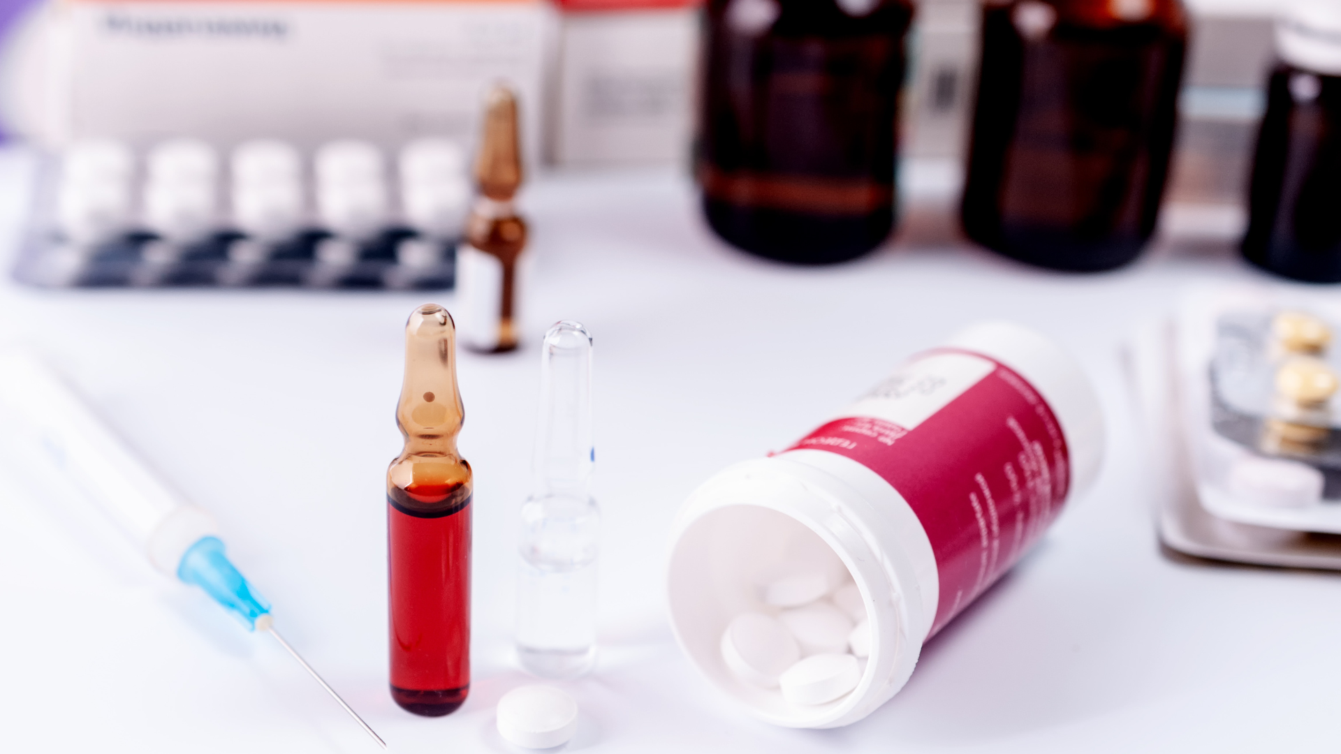 Small ampule, red vial, syringe, and white medicine bottle on a lab countertop