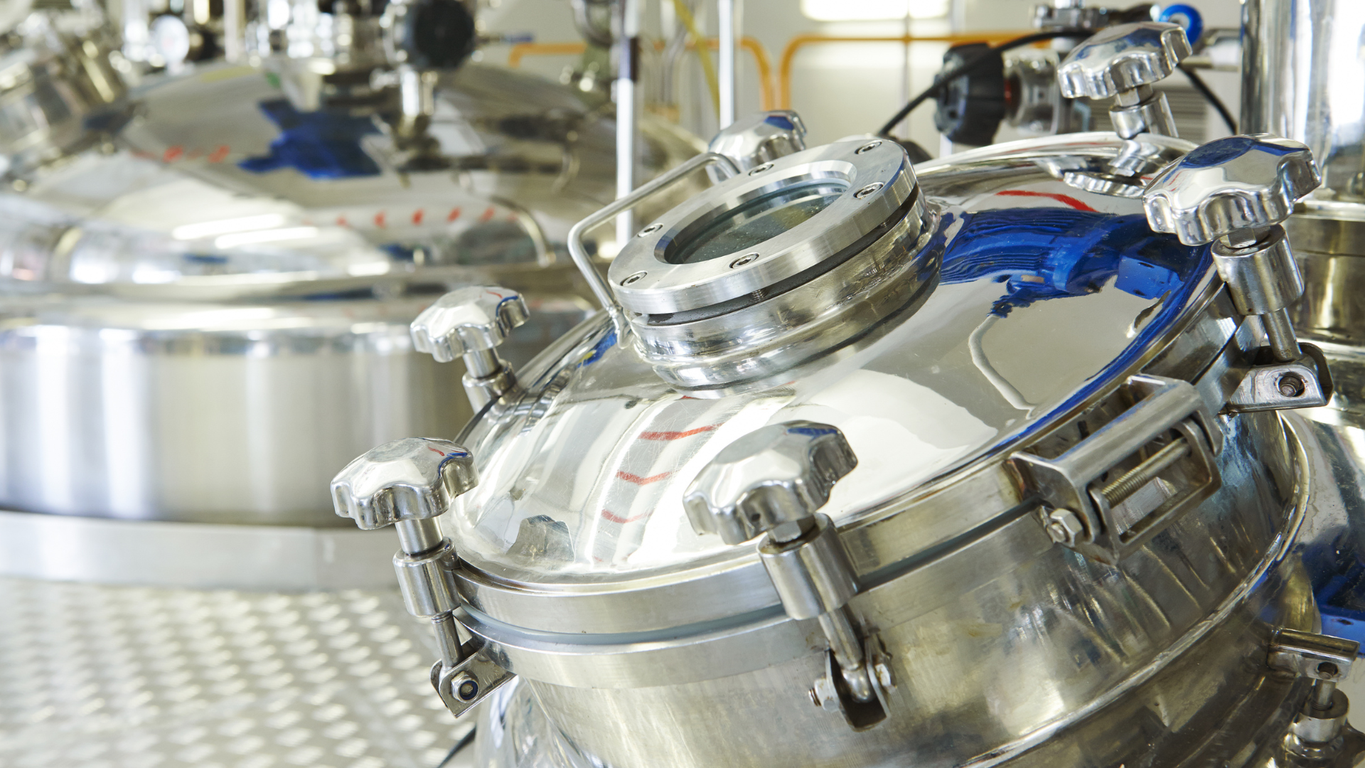 Polished stainless steel industrial tanks and piping in a bright factory setting