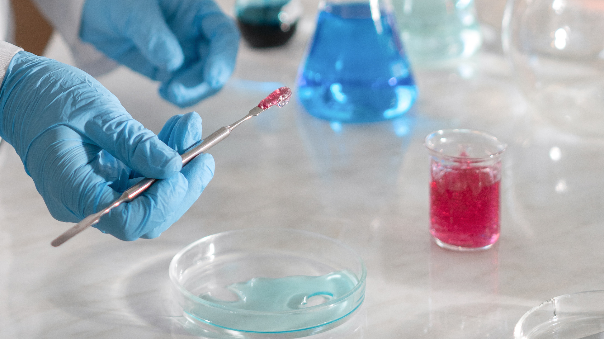 Gloved hand holding a swab in a lab, with petri dishes and colored sample containers on a countertop