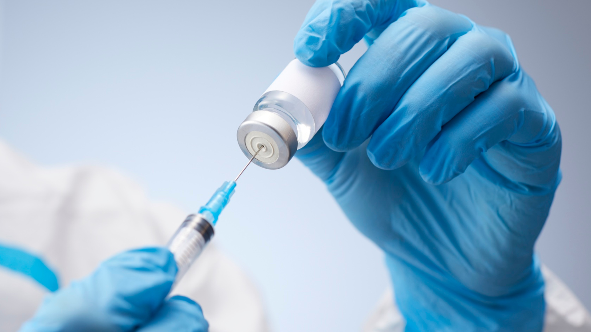 Gloved hands preparing a syringe from a vaccine vial in a clinical setting