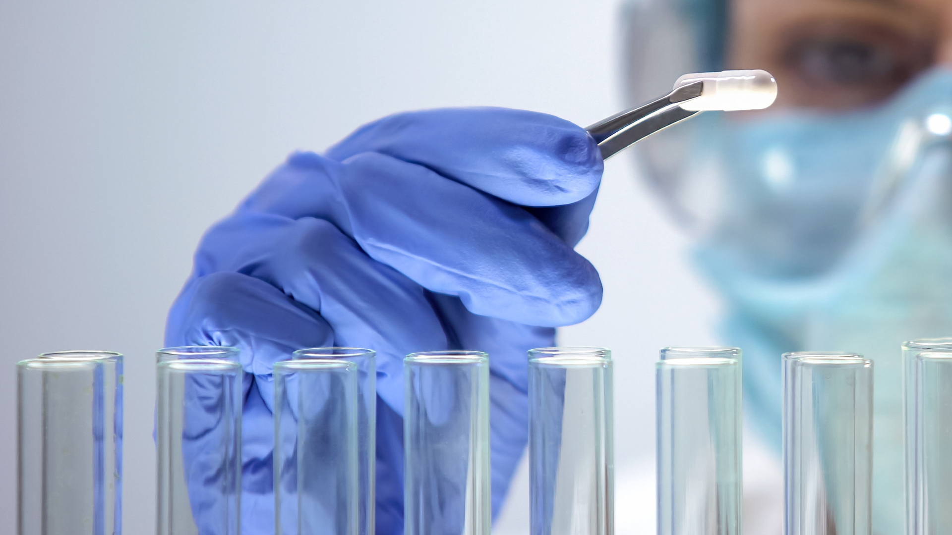 Gloved lab worker holding a swab over test tubes in a clinical setting