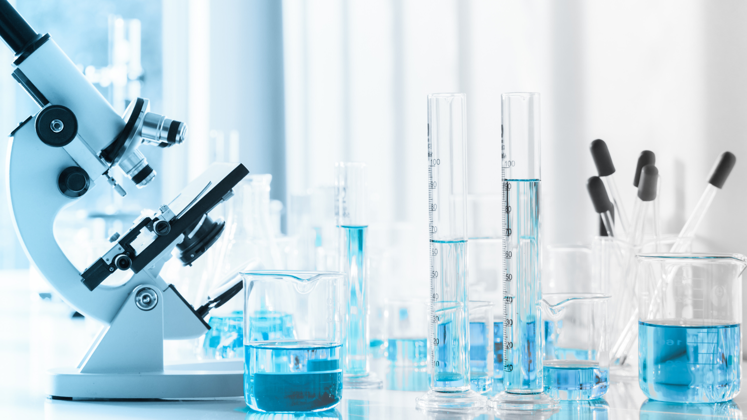 Microscope and glass labware with blue liquid in a bright laboratory setting