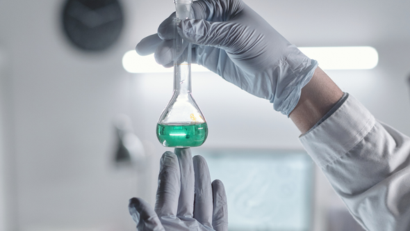 Gloved scientist holding a flask with green liquid in a lab setting