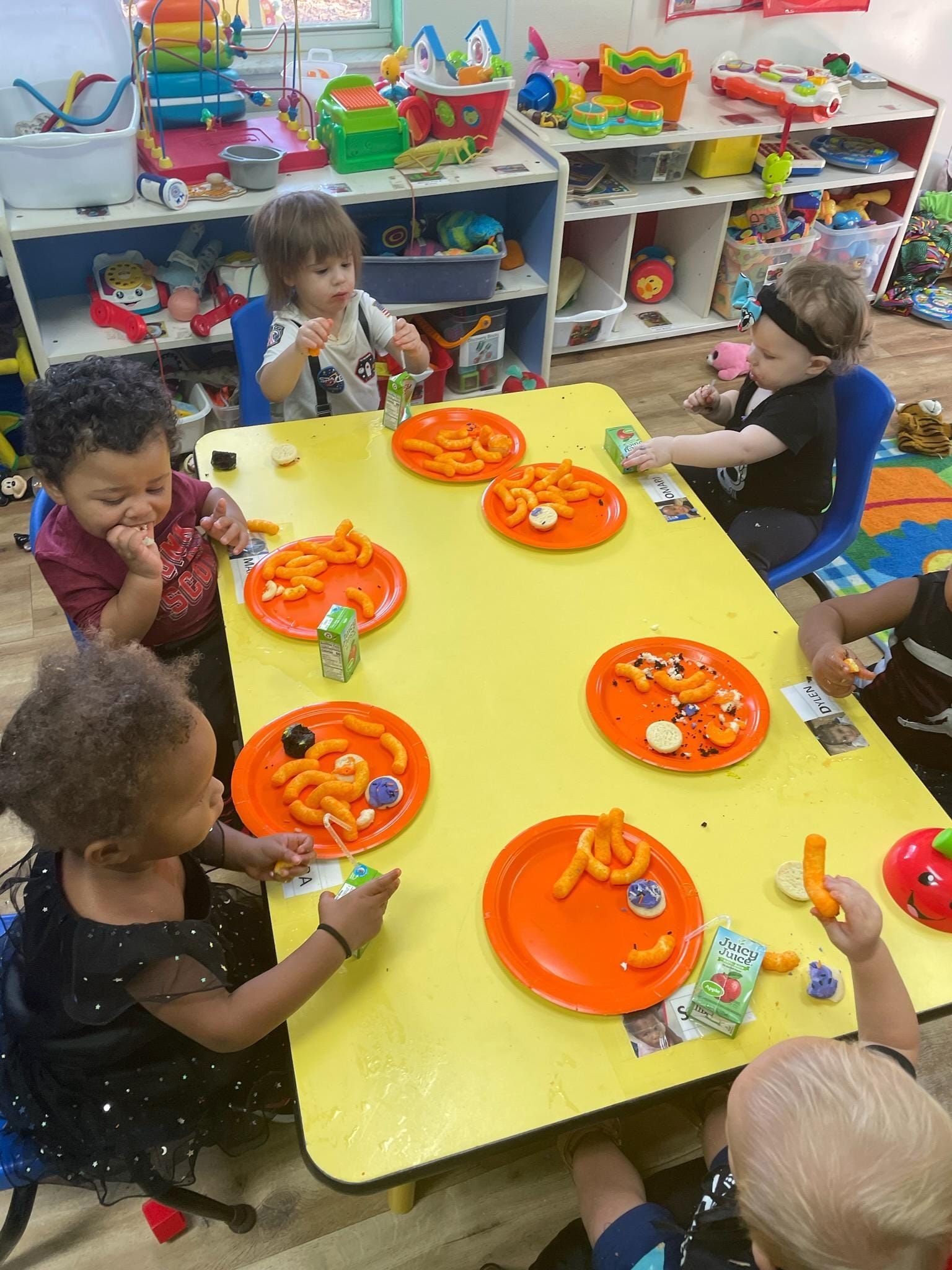 A group of children are sitting at a table with plates of food on it.