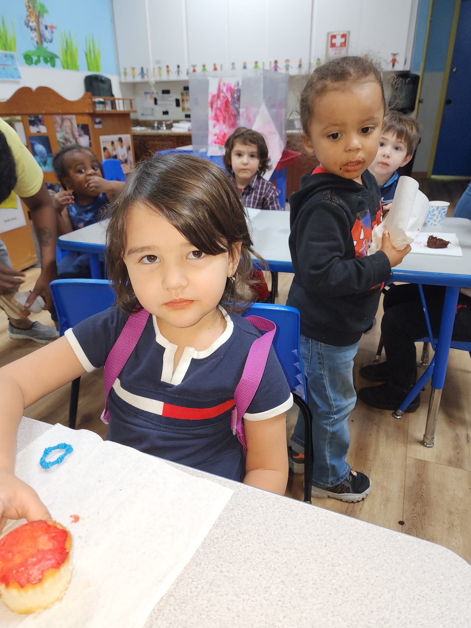 A girl with a backpack is sitting at a table with other children