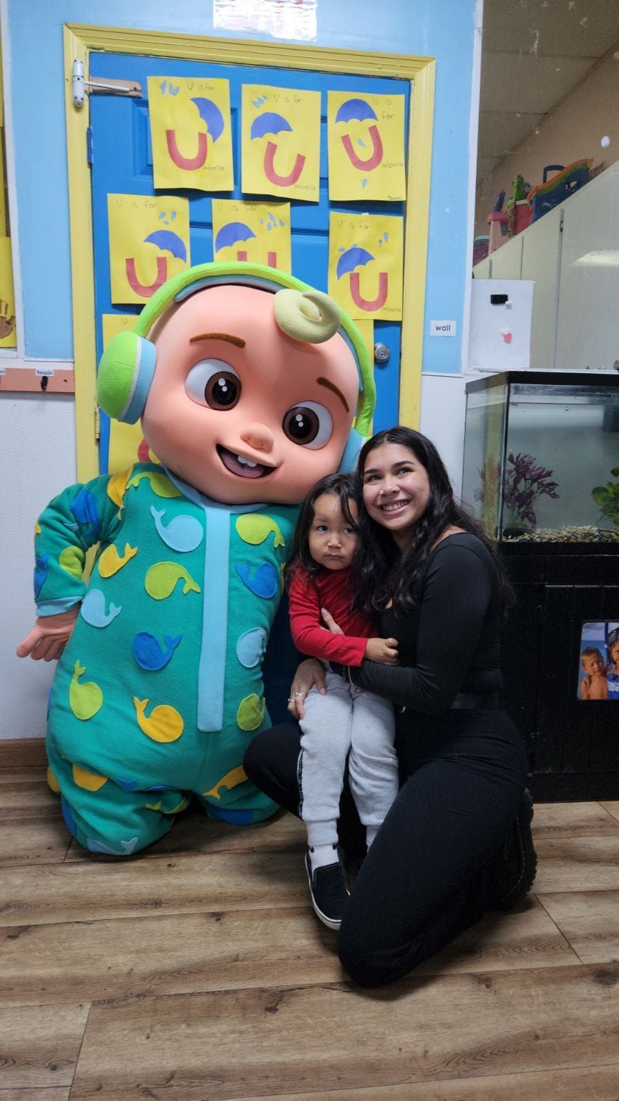 A woman is kneeling down next to a baby cocomelon mascot