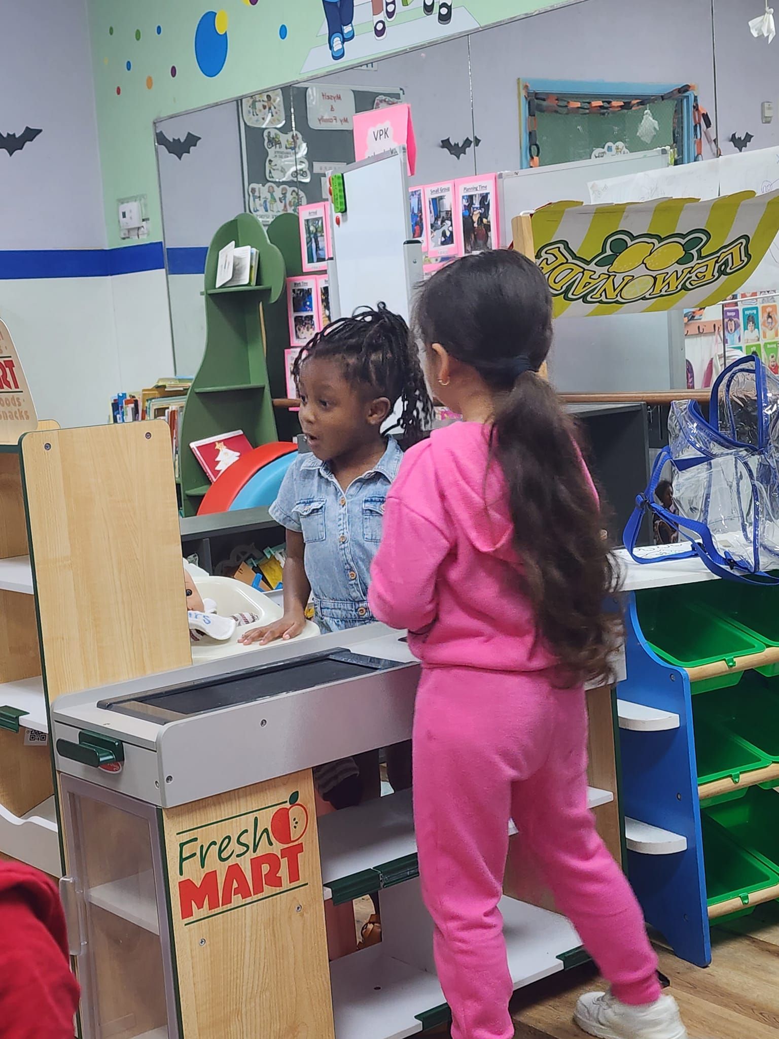Two little girls are standing next to each other in a play room.