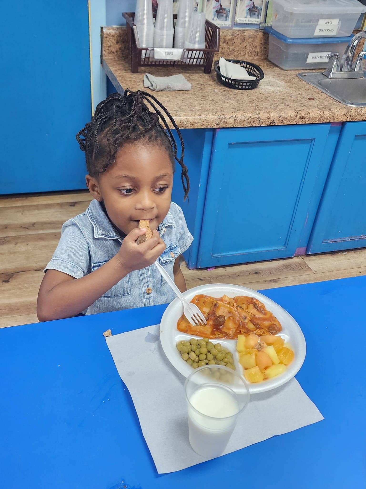 A little girl is sitting at a table eating a plate of food.