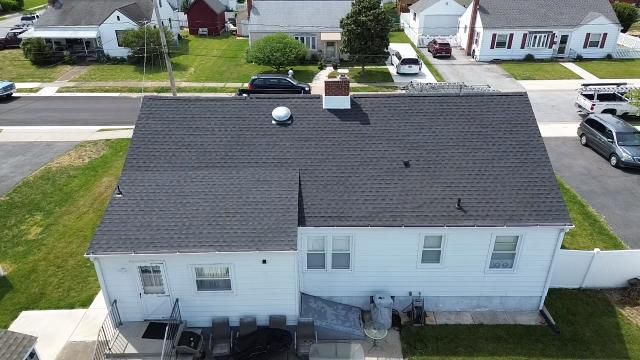 An aerial view of a white house with a black roof in a residential neighborhood.