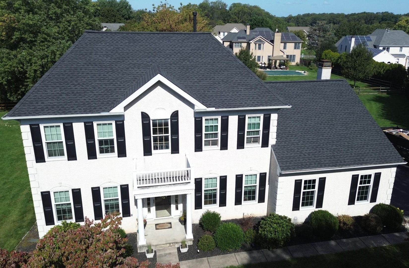 White two-story house with black shutters and dark gray roof in a suburban setting.