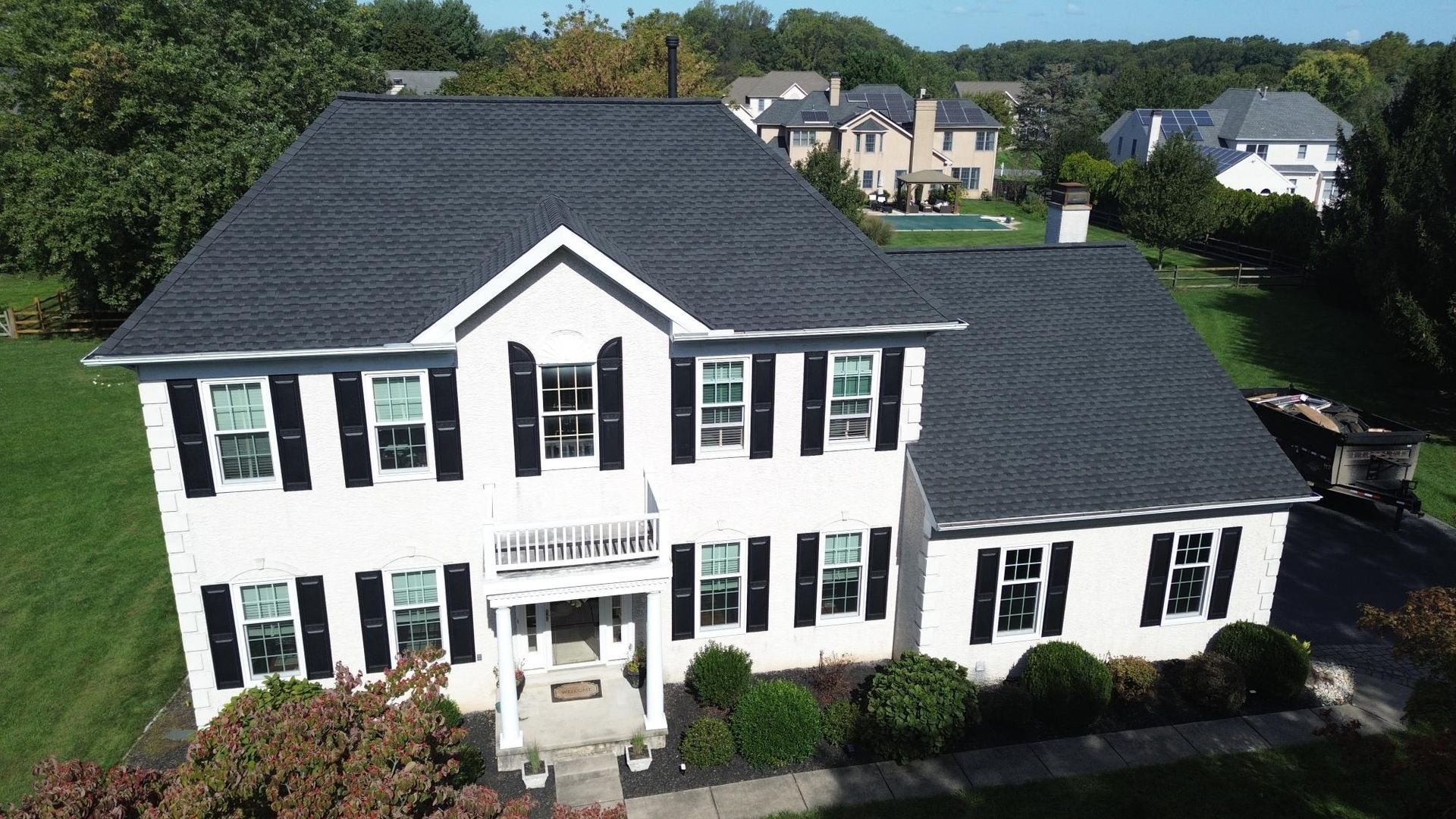 White two-story house with black shutters and dark gray roof, surrounded by green grass and trees.
