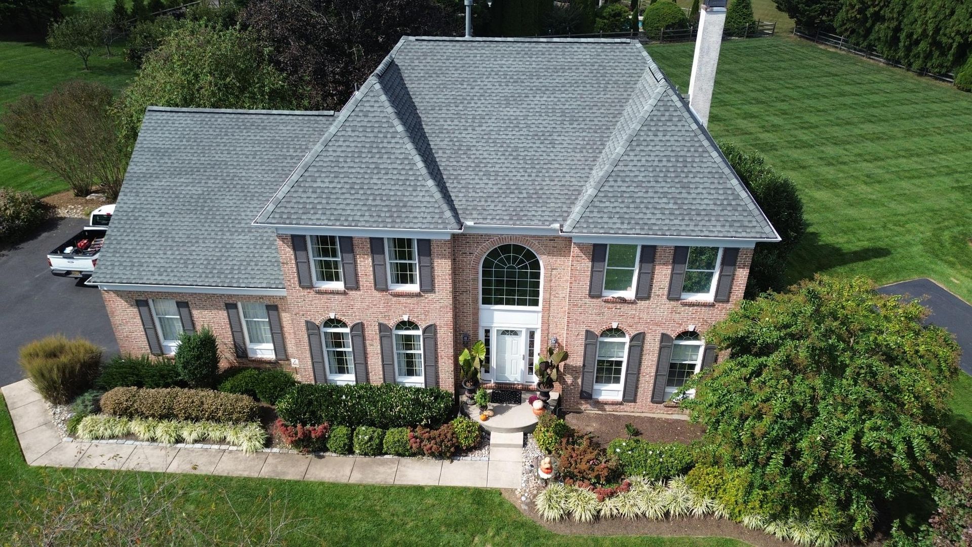Brick house with a gray roof and numerous windows. Front door flanked by landscaping, with a green lawn.