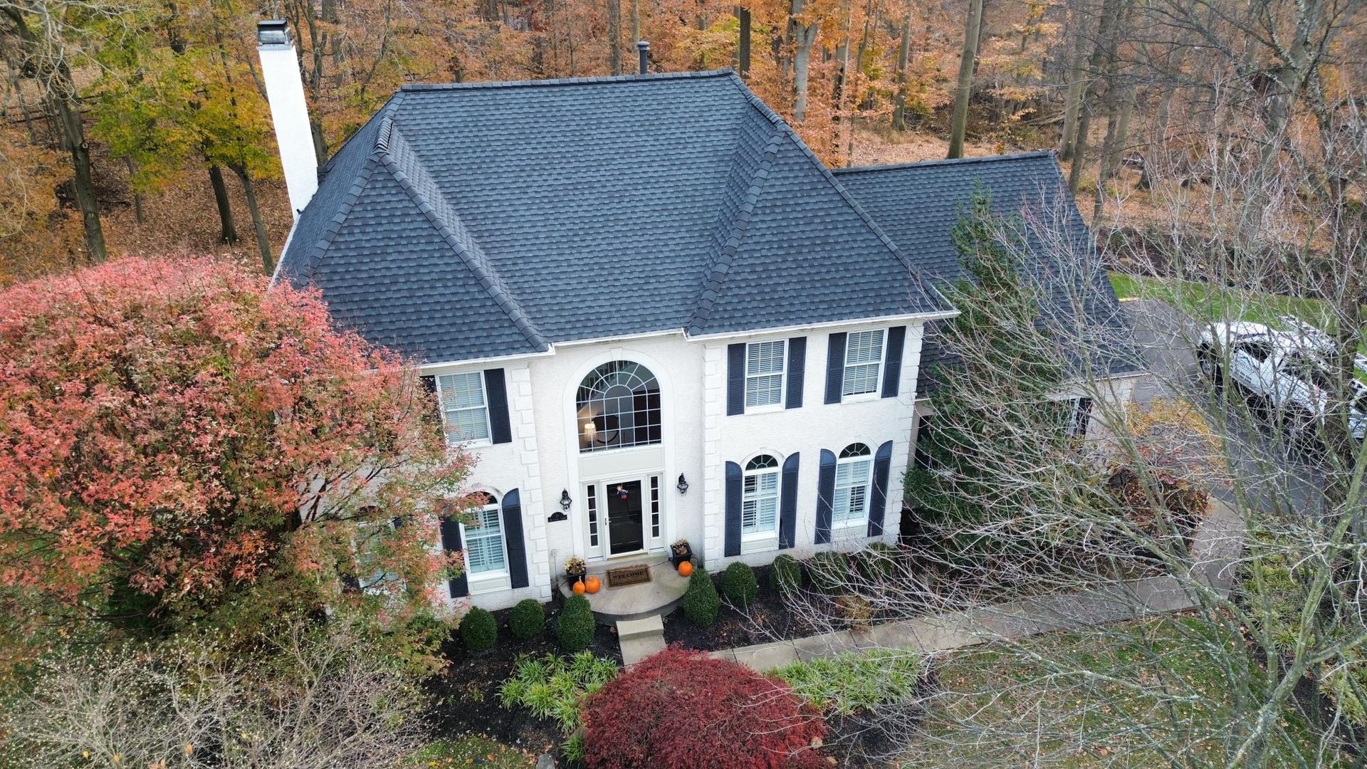 Two-story white house with black roof and shutters, surrounded by fall foliage.