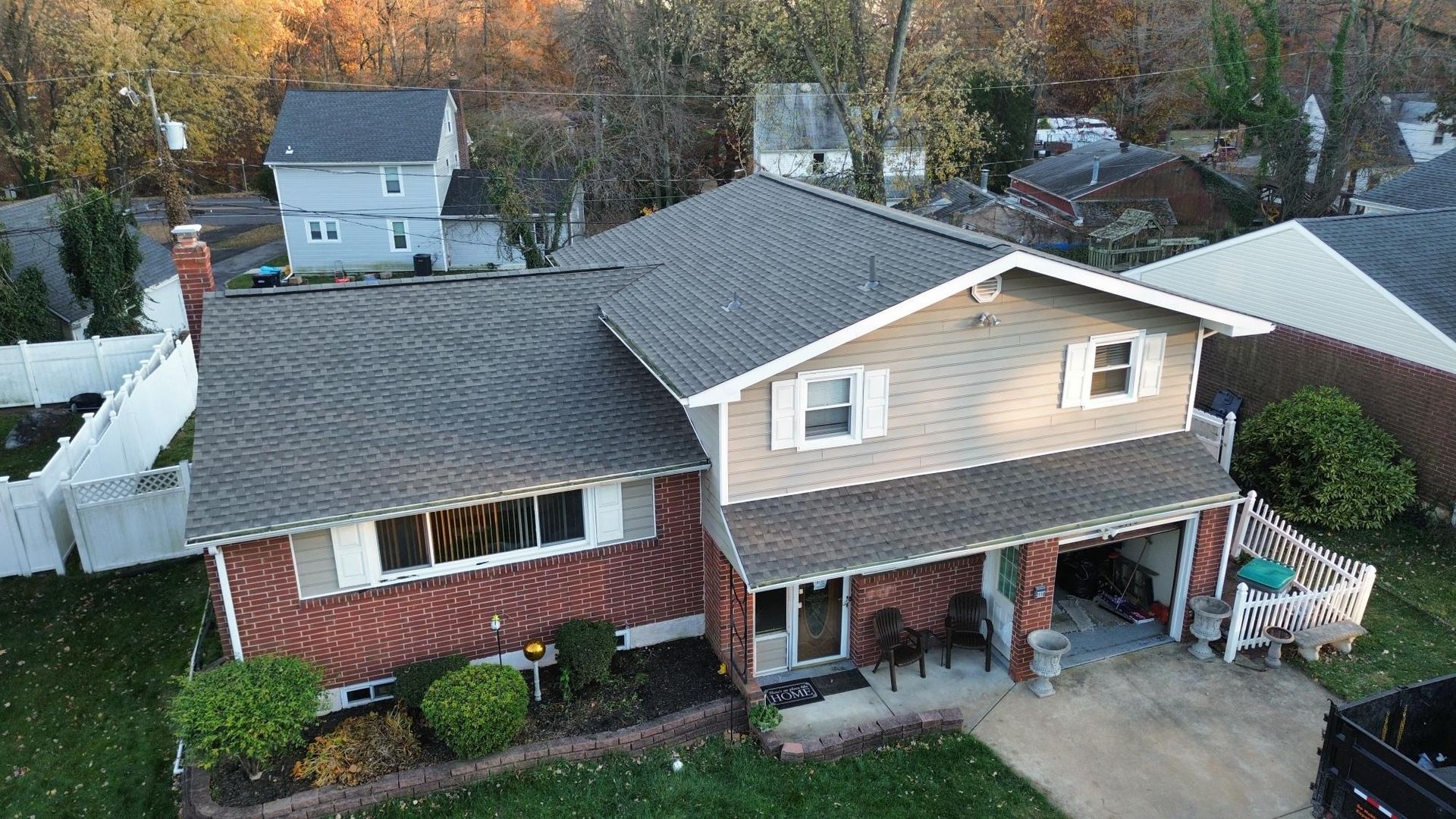 Overhead view of a two-story house with a brick facade and gray roof; trees and other houses in the background.