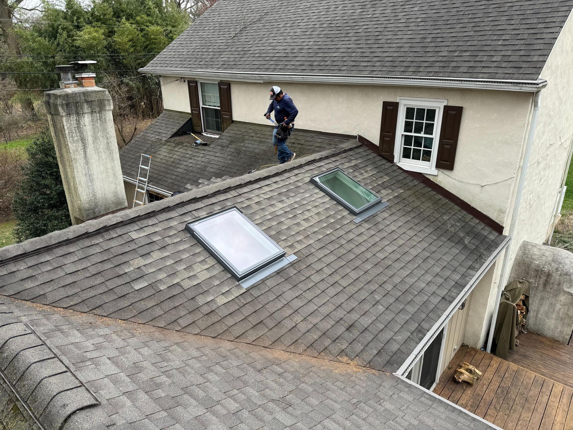 A man is standing on the roof of a house with two skylights.
