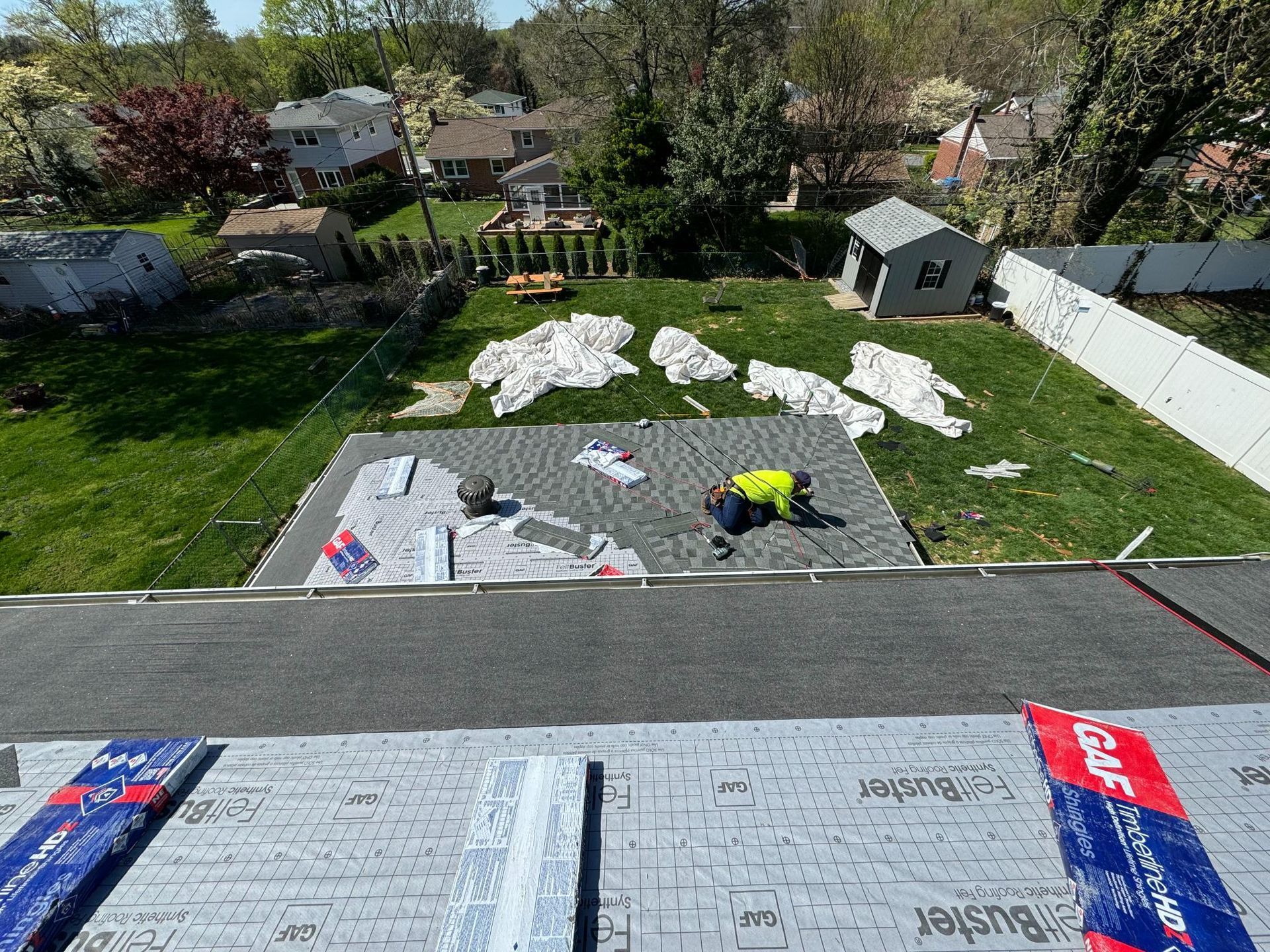 A man is laying shingles on a roof in a backyard.
