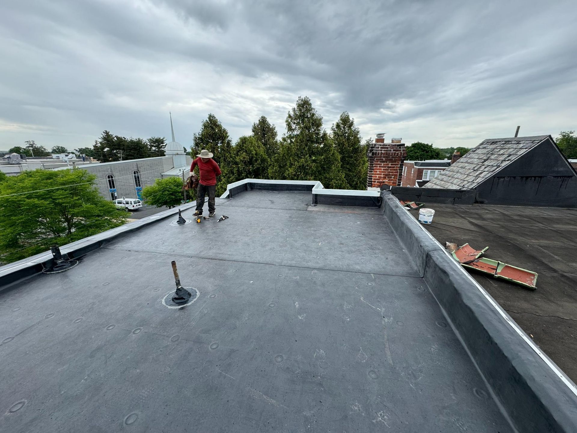A man is standing on top of a roof with a broom.