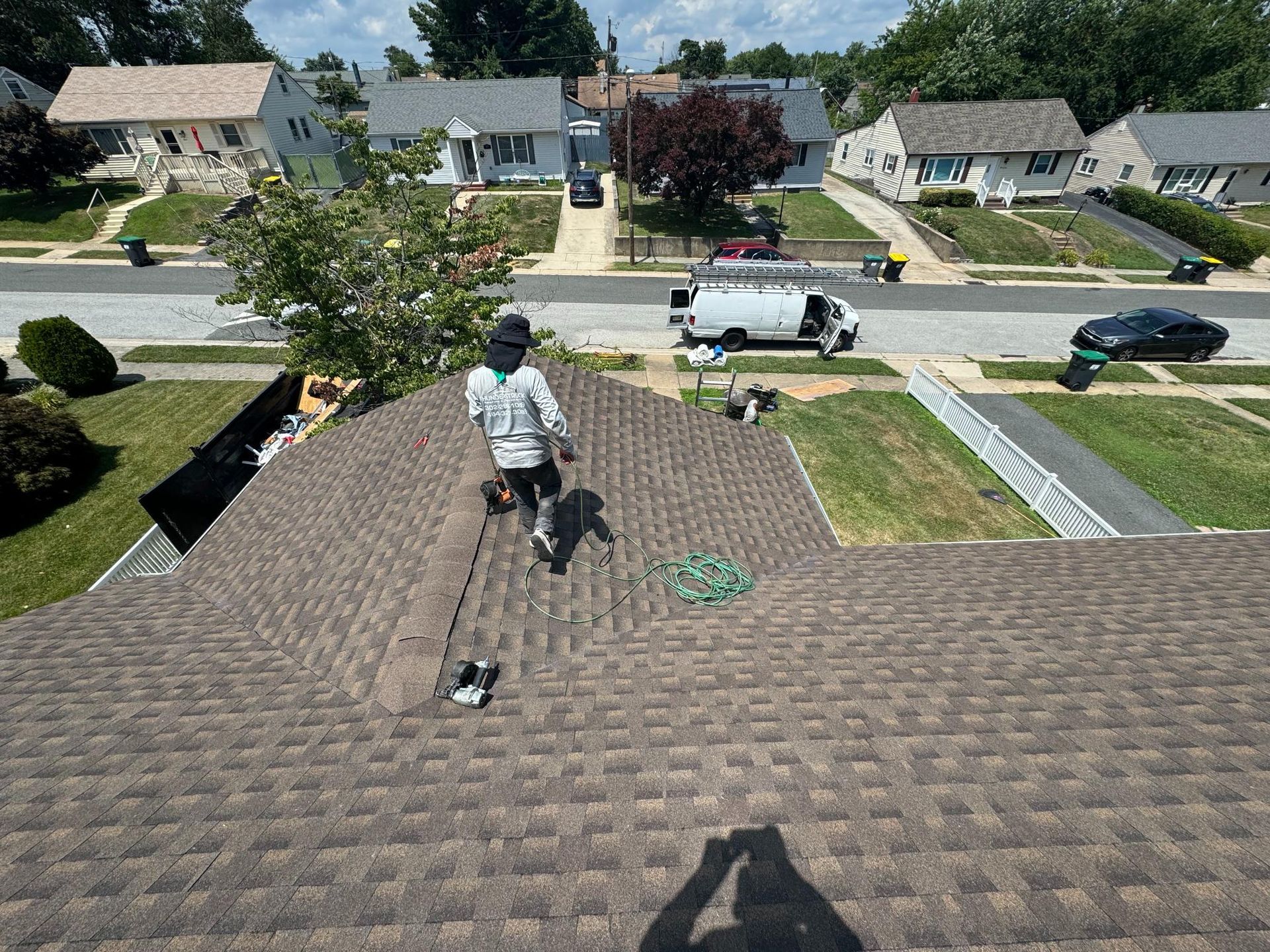 A man is standing on top of a roof in a residential neighborhood.