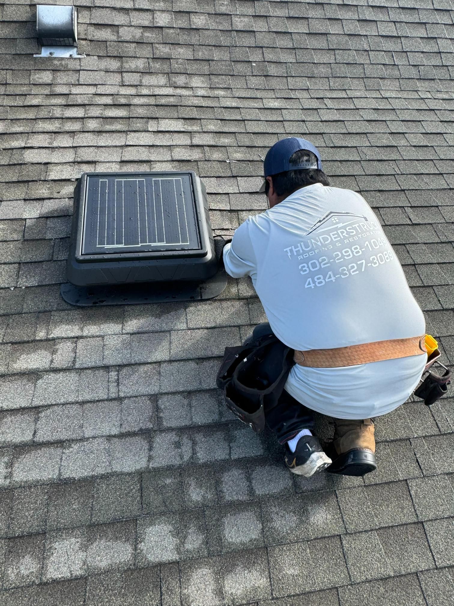 A man is kneeling on a roof working on a solar panel.
