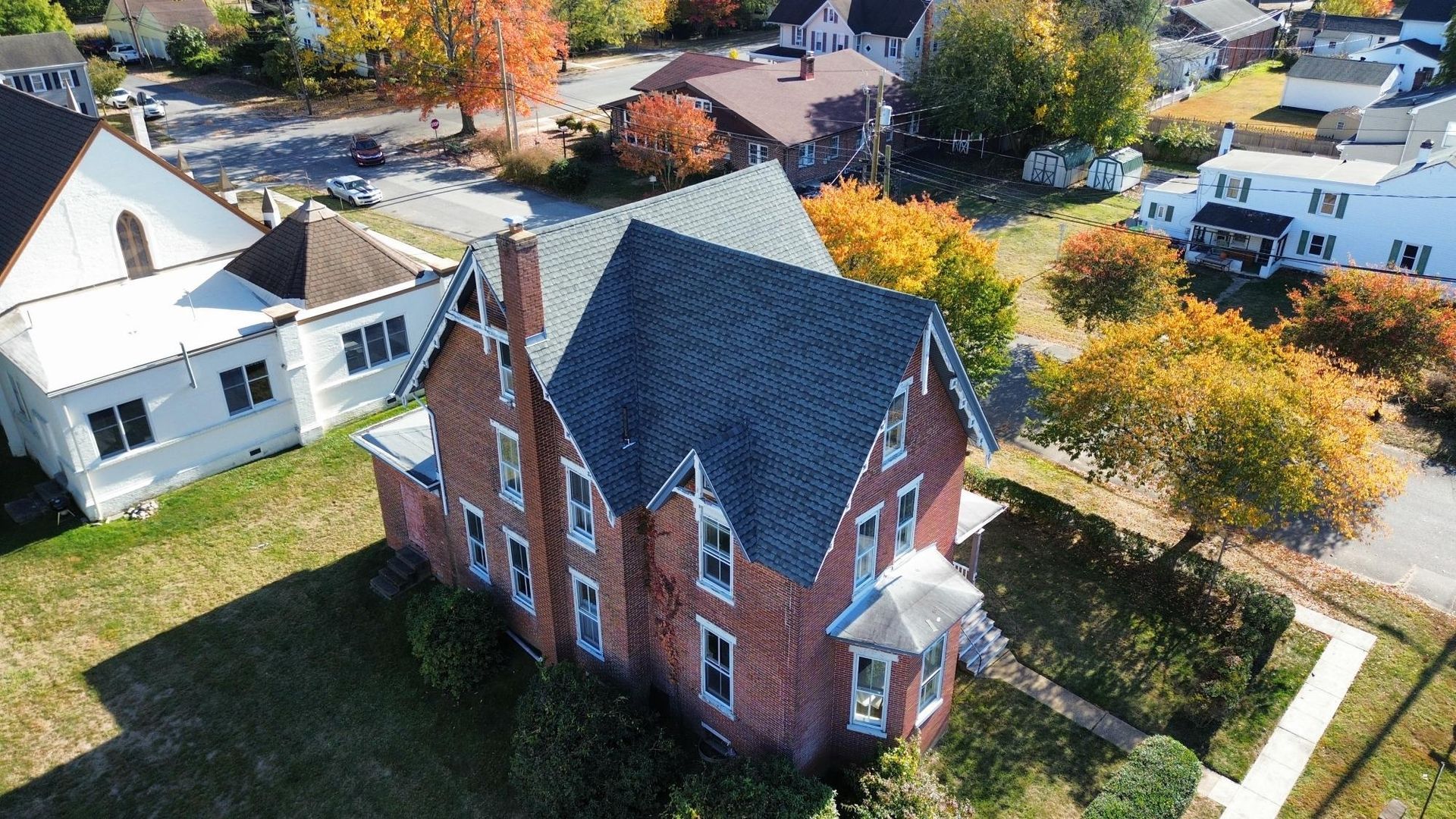 An aerial view of a brick house with a black roof in a residential area.