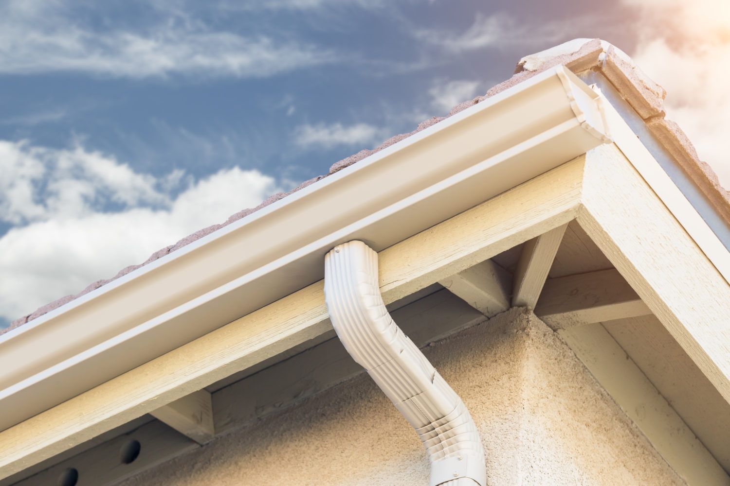 A white gutter on the side of a house with a blue sky in the background.
