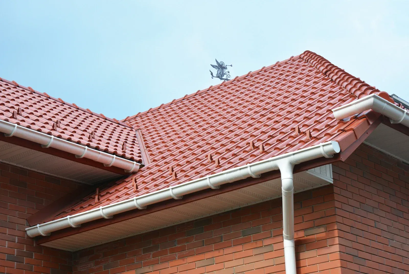 A brick house with a red tiled roof and a white gutter.