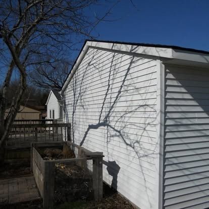 White building with tree shadow, blue sky. Deck and compost bin in front.
