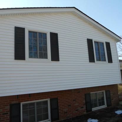 White house with black shutters and brick foundation.