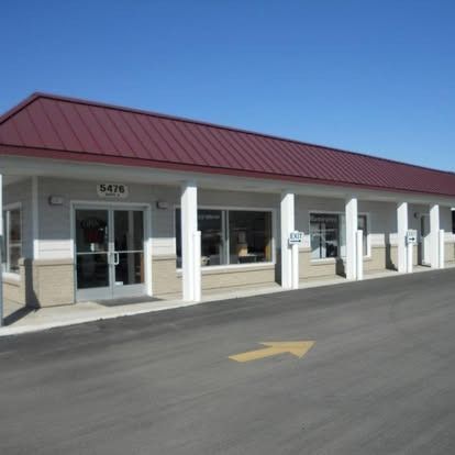 Building with maroon roof, white pillars, windows, and a yellow arrow on the pavement.
