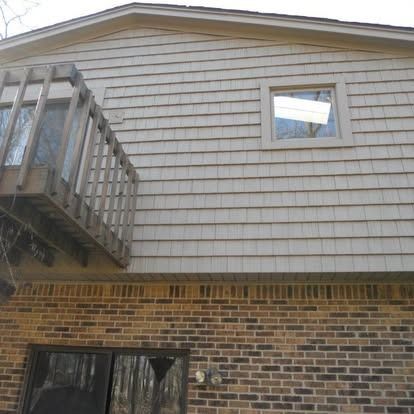 Exterior view of a house with a wooden deck, brick base, and shingle siding.