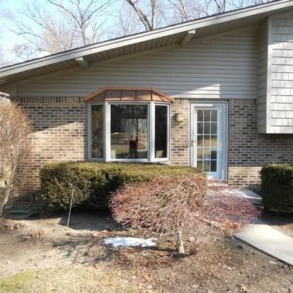 Exterior view of a brick house with a bay window, front door, and shrubs.