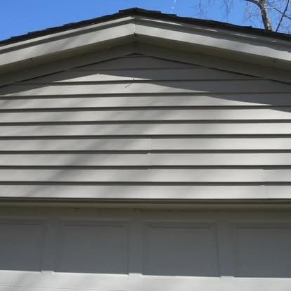 Garage exterior with light-colored siding and a dark roof.