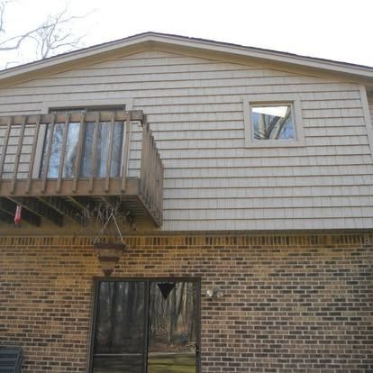 Building with brick base, wooden deck, and siding; door and window visible.