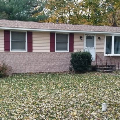 Ranch-style house with tan siding, brick facade, burgundy shutters, and a lawn covered in fallen leaves.
