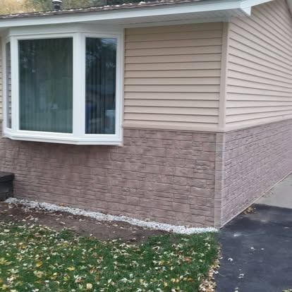 House exterior with tan siding and brick-like lower section, bay window, and lawn.