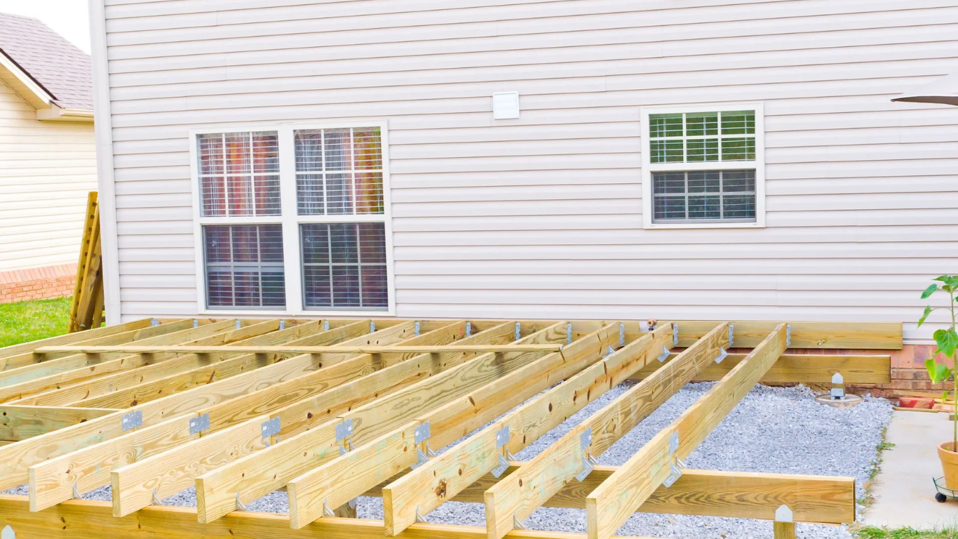 Wooden deck frame under construction near a house with windows.