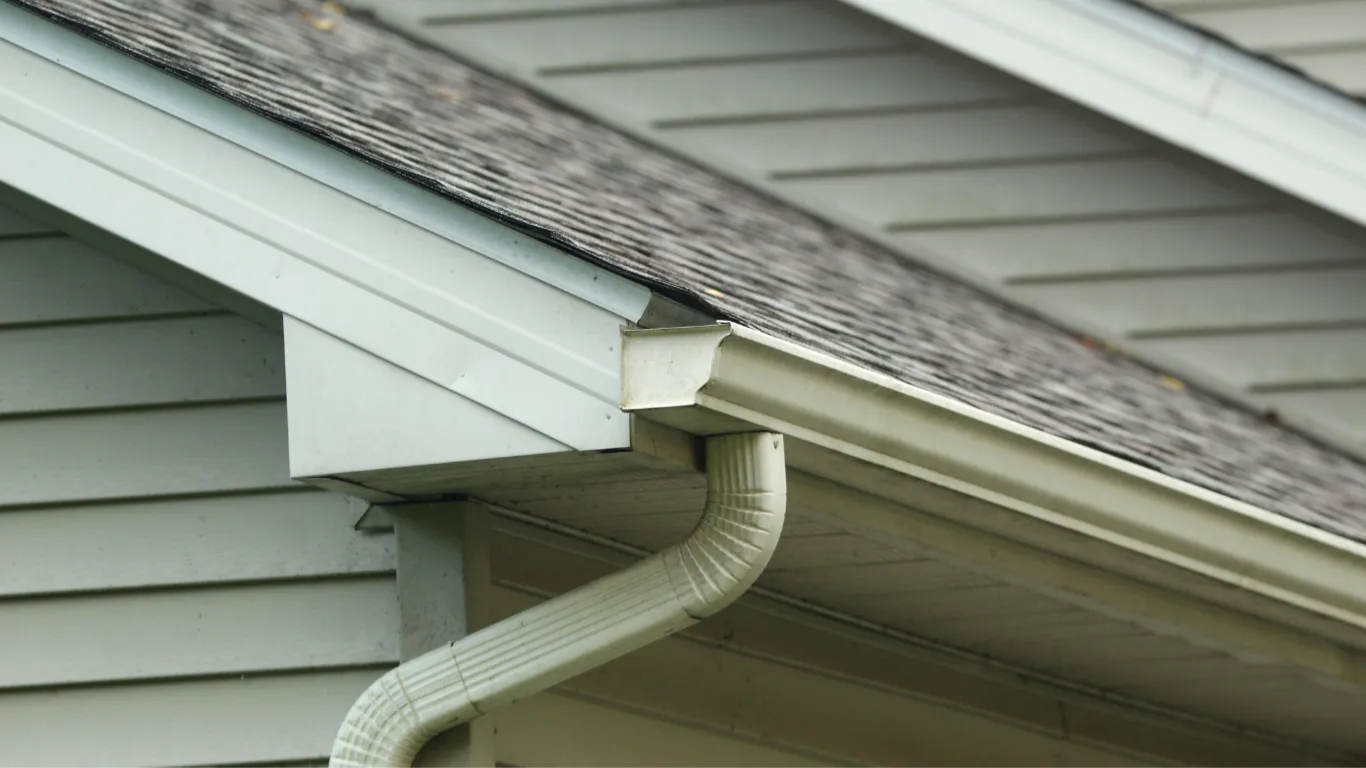 Light blue gutters and downspout on a house with gray siding and roof.