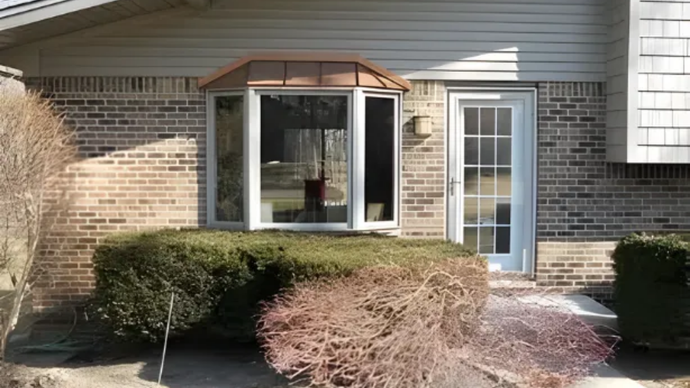 Exterior view of a brick house with a bay window, front door, and shrubs.