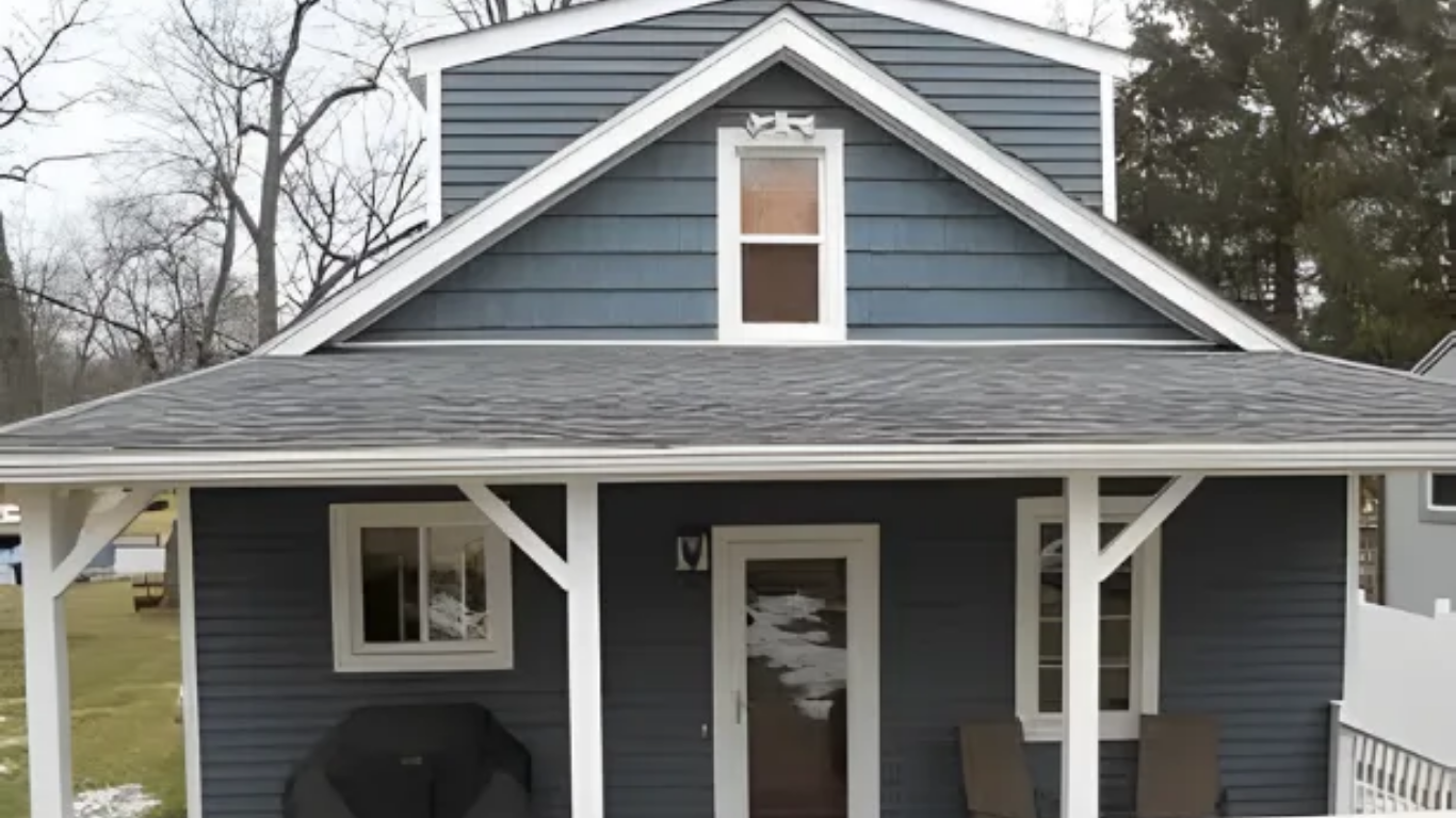 Blue house with white porch, brown deck, and small bushes.